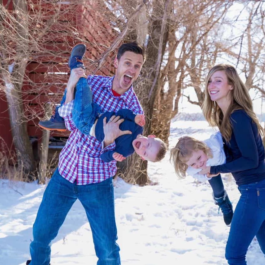 Happy family playing outdoors in the snow, promoting chiropractic care, wellness, and healthy living.